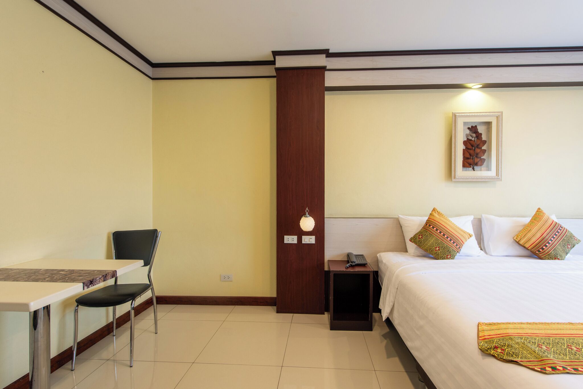 A hotel room with a bed, a desk with a chair, a nightstand, and a wall-mounted lamp.