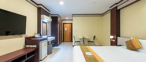 A hotel room with a bed, a desk, a television, a small kitchenette, and a bathroom.