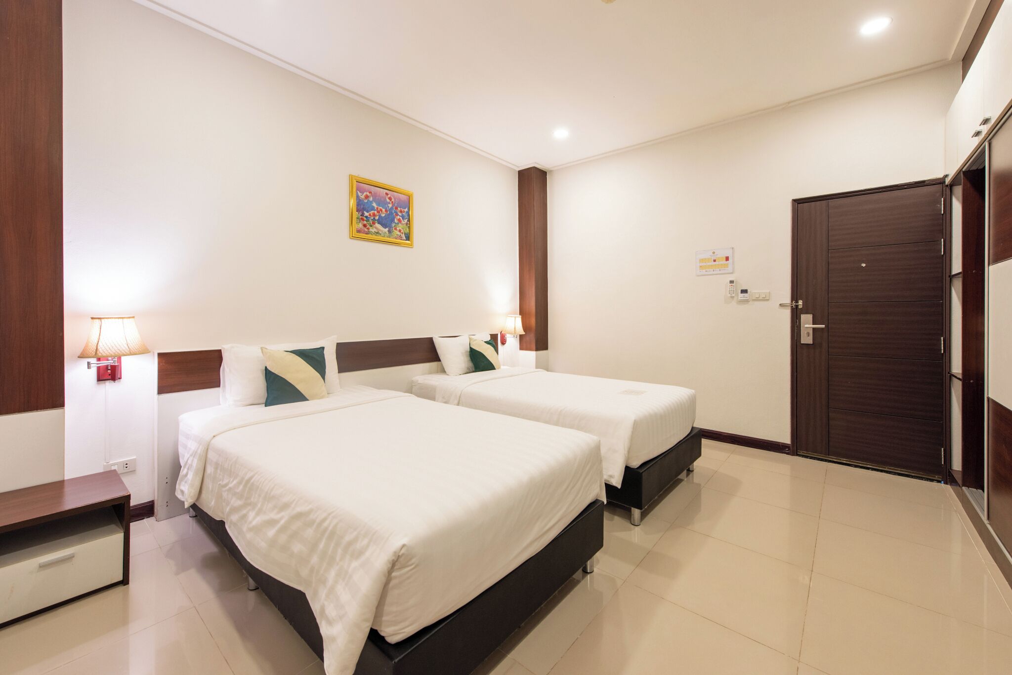 A hotel room with two beds, a nightstand, a lamp, a painting, and a door.