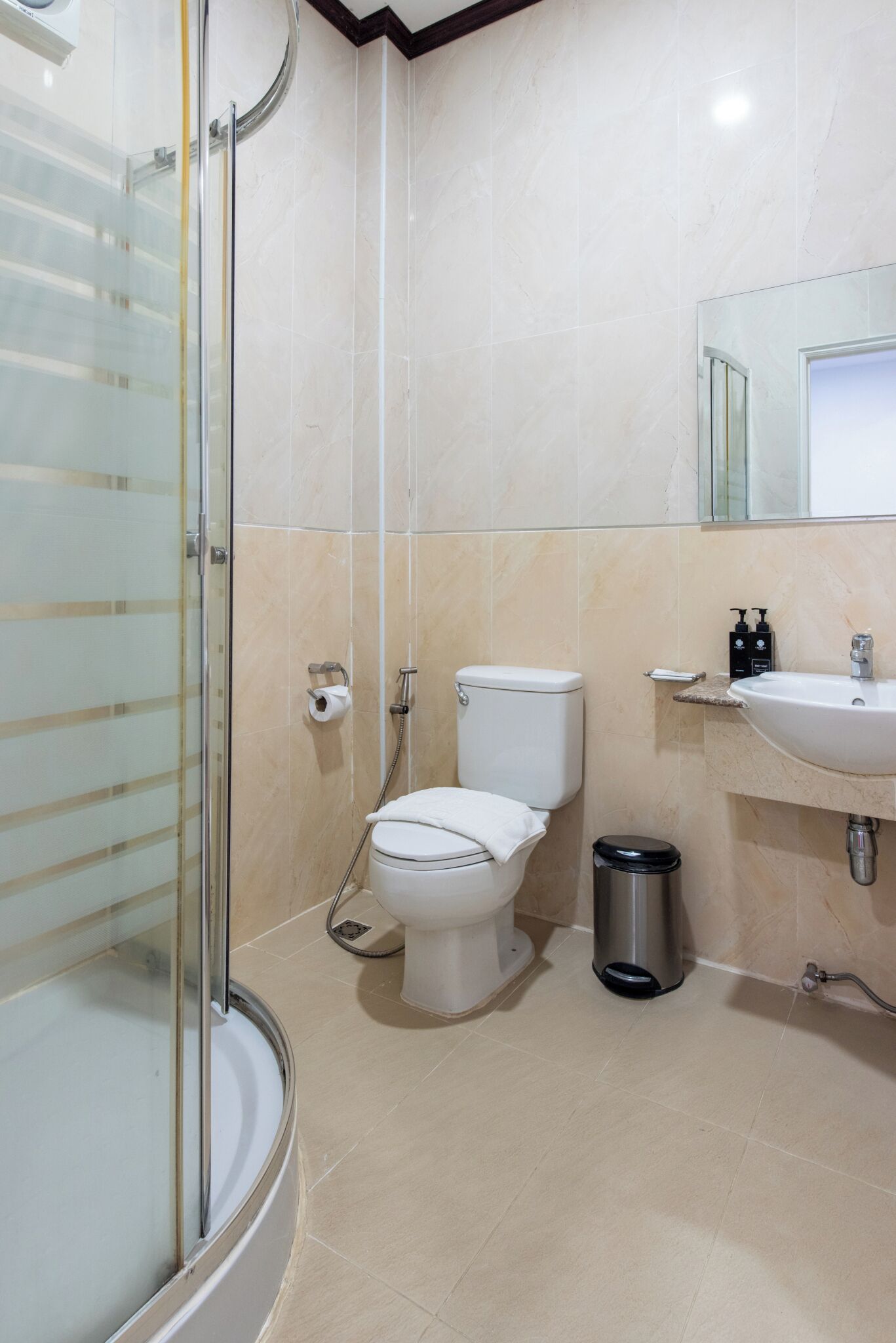 Une salle de bain avec une douche à parois de verre, des toilettes, un lavabo et une poubelle.