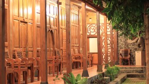 A wooden structure with multiple seating areas and a stone wall. - Pendhapa Art Space - PAS Limasan Homestay (Sewon)