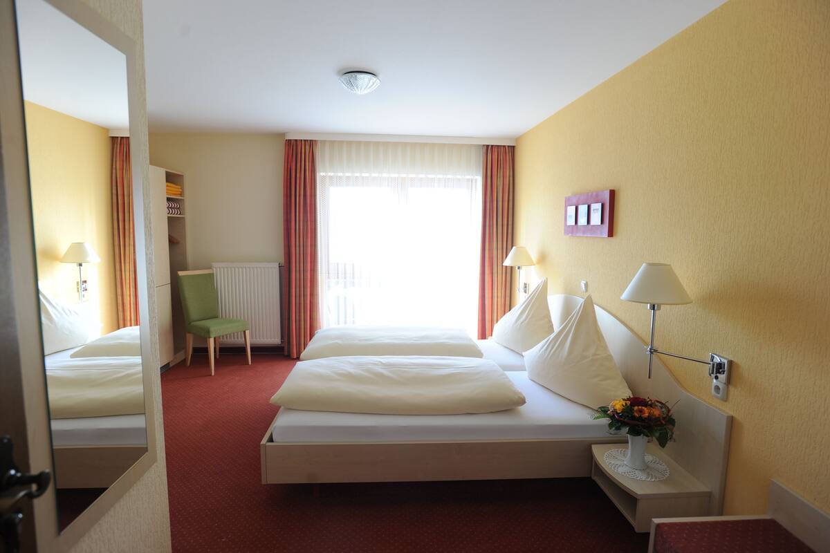 A hotel room with a large bed, two bedside tables, a chair, a radiator, and a window with curtains.