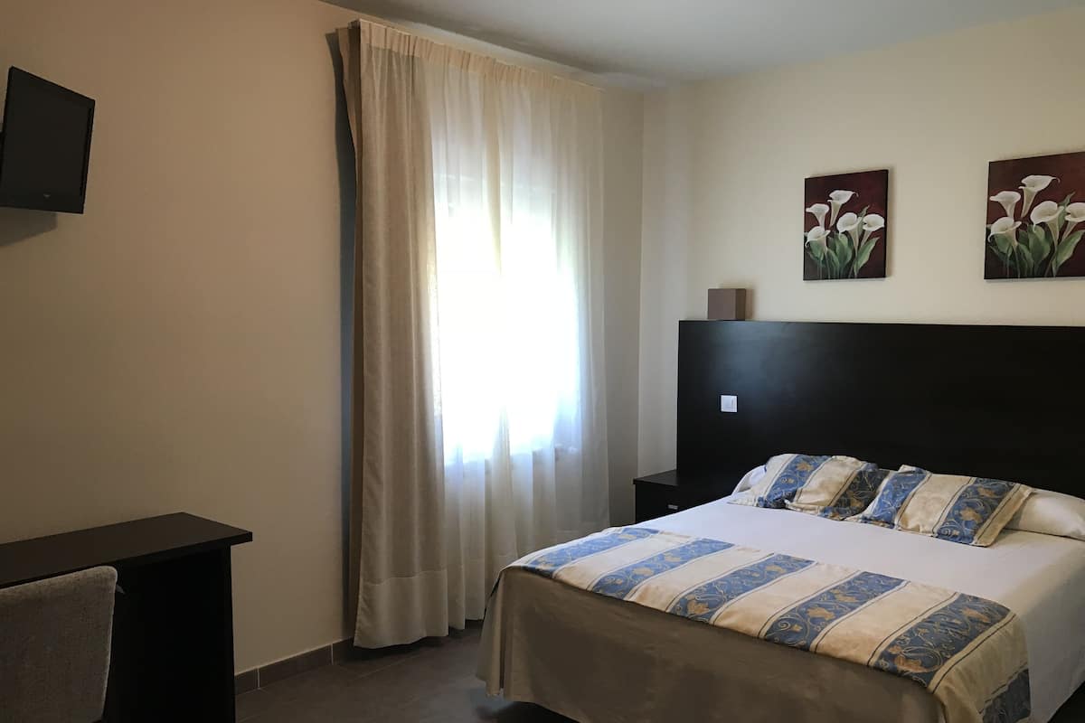 Habitación de hotel con cama, escritorio, silla, televisor en la pared y dos cuadros.