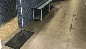 A public restroom with blue-tiled walls, multiple sinks, benches, and a central area with a hot tub.