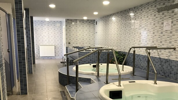 A spa area with two hot tubs, tiled walls, and a tiled floor.