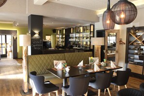 Un ristorante con un'area bar, una zona con tavolo ad alto schienale e un espositore di bottiglie e bicchieri.