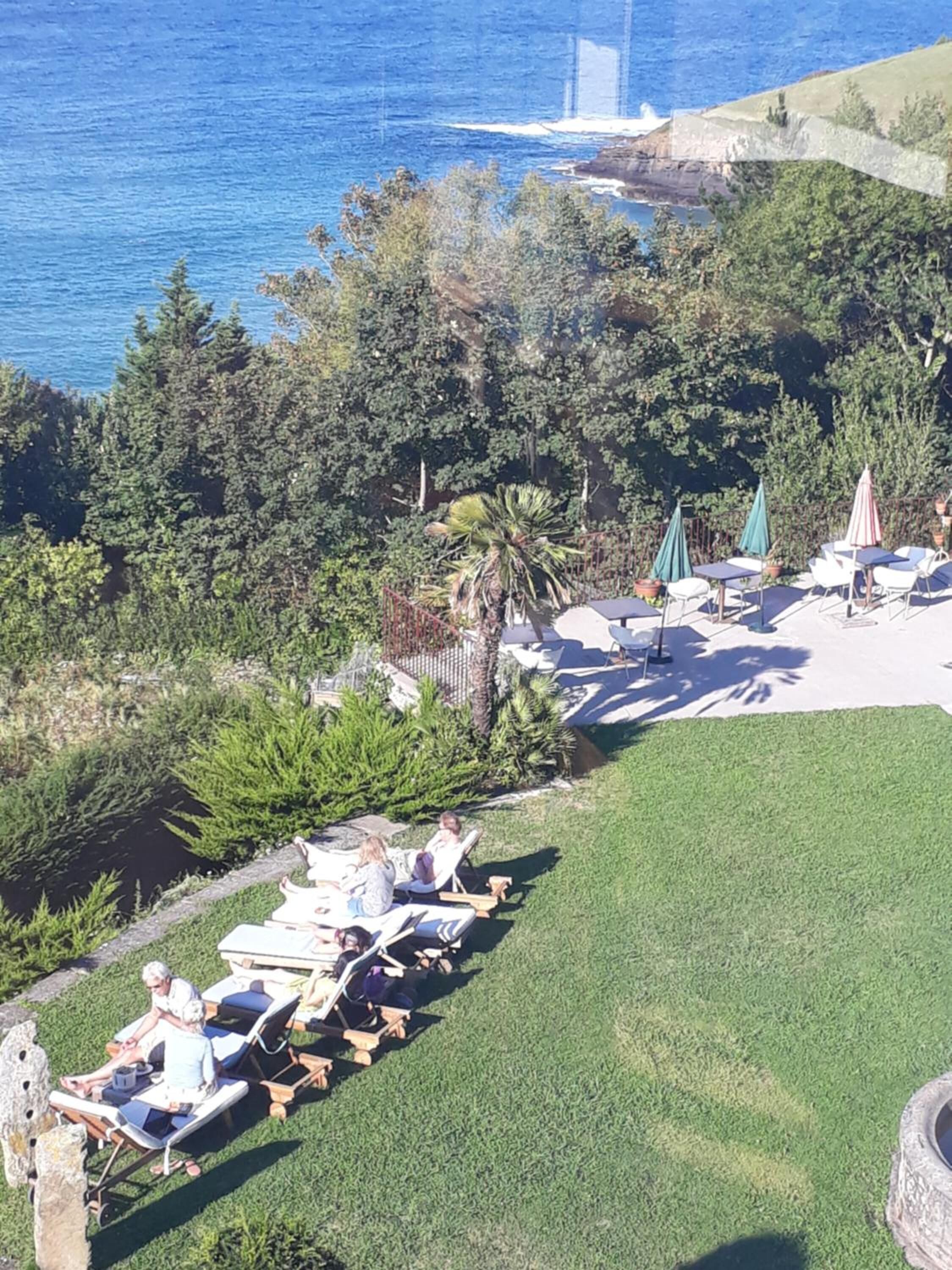 A patio area with lounge chairs and umbrellas, overlooking a body of water and a rocky coastline.