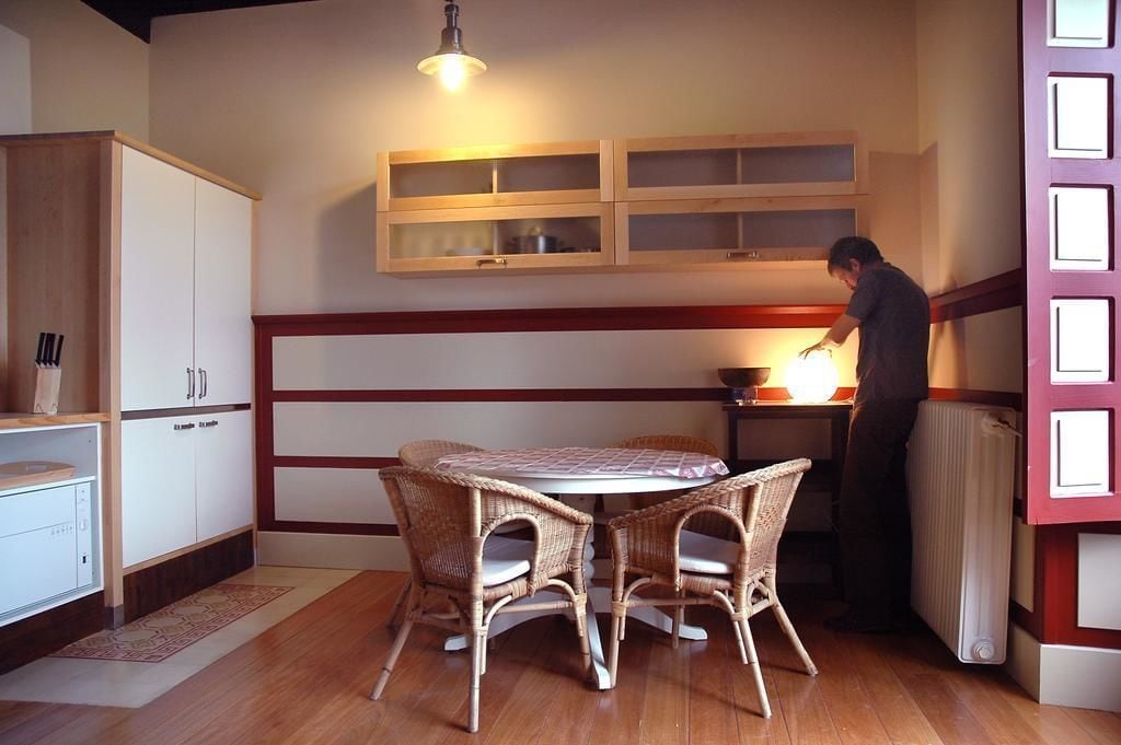 Un comedor con sillas de mimbre y una mesa, un mueble de madera con cajones y un radiador.