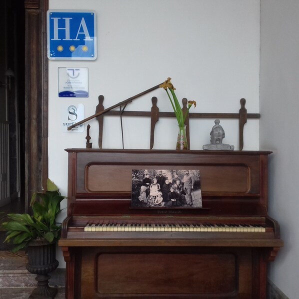 A piano with a family photo, a blue sign with 'HA' and sun symbols, and a plaque.