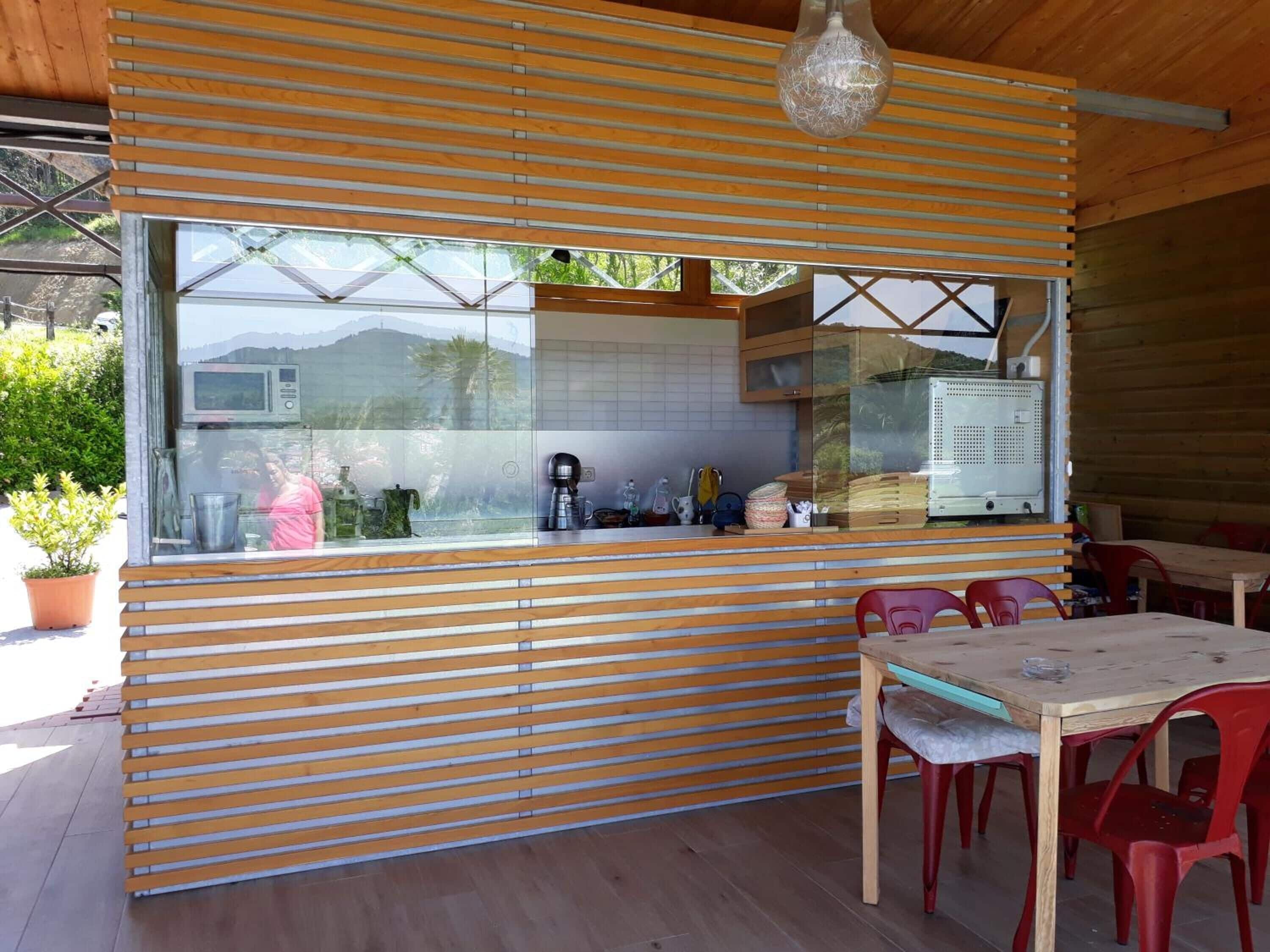 A modern kitchen with wooden slats, a large window, and a dining area with red chairs.