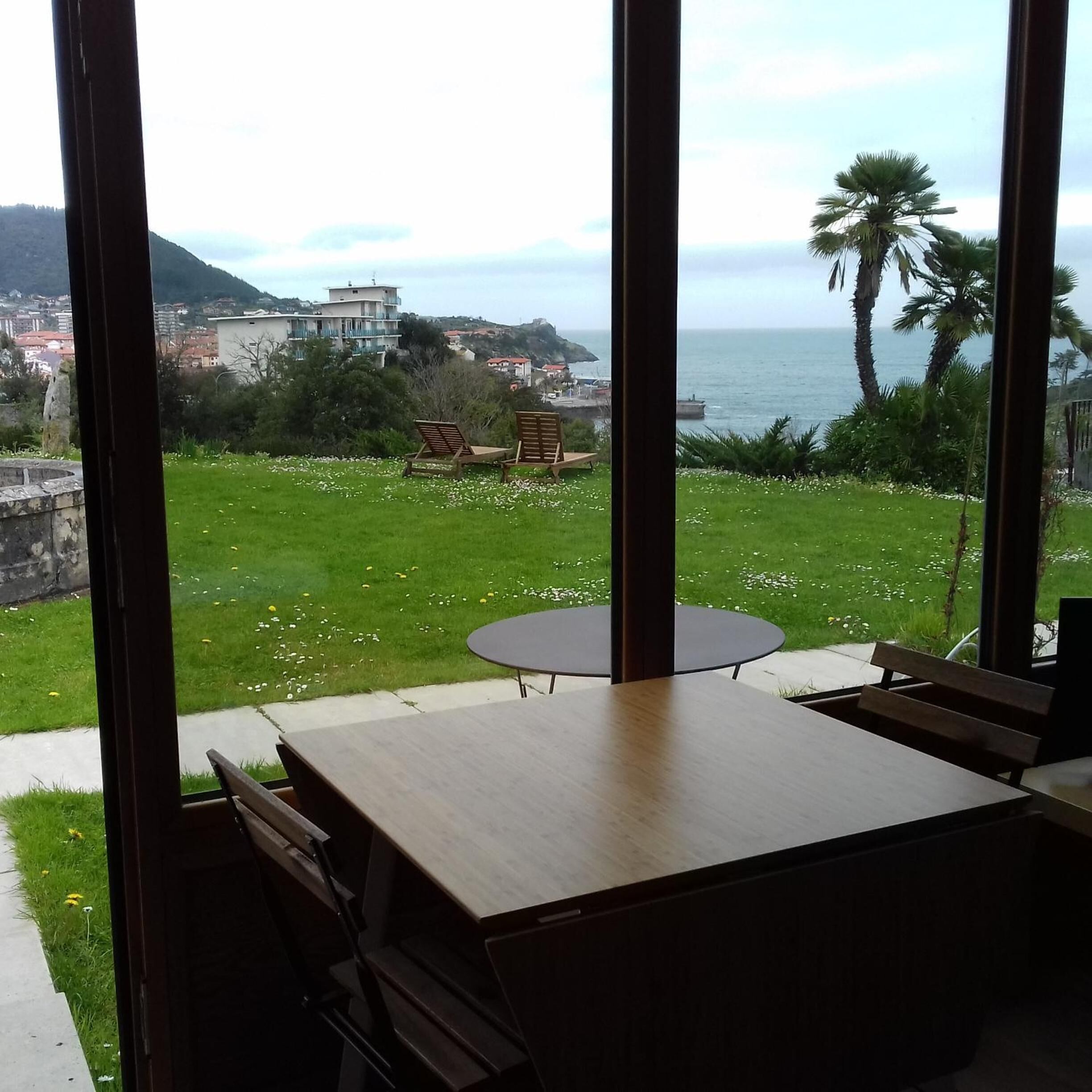 A dining area with a table and chairs, overlooking a grassy lawn and a coastal view.