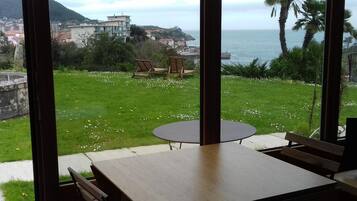 A dining area with a table and chairs, overlooking a grassy lawn and a coastal view.