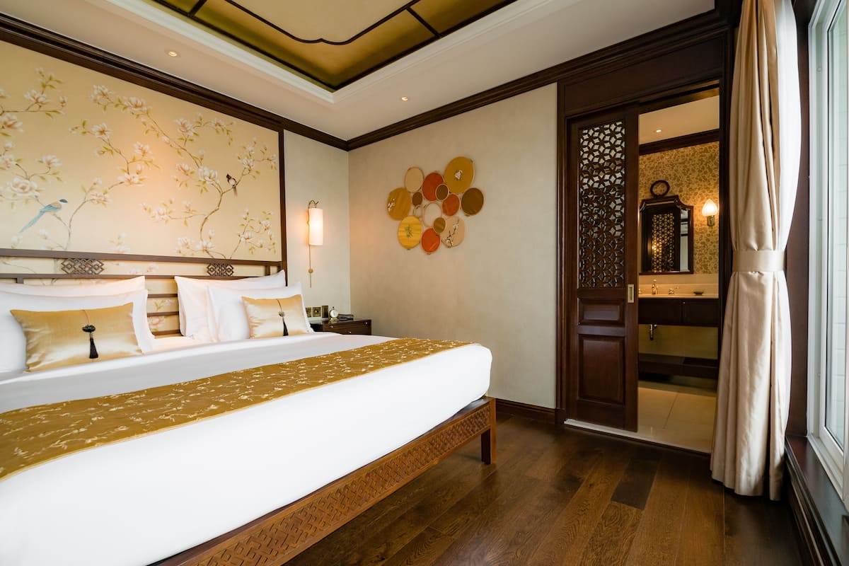Ein Hotelzimmer mit einem großen Bett, einer Wand mit dekorativen Kreismustern, einer Holzbank und Blick auf ein Badezimmer durch eine offene Tür.