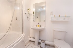 Uma casa de banho com chuveiro envolto em vidro, lavatório assentado, sanita e espelho sobre o lavatório.