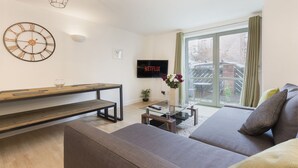 A modern living room with a sofa, a glass coffee table, a wooden bench, a wall-mounted clock, and a TV displaying "NETFLIX". - Raleigh Square Apartments (Nottingham)