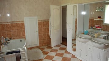 Uma casa de banho com chão quadriculado, banheira, toucador com duas pias e espelho sobre a pia.