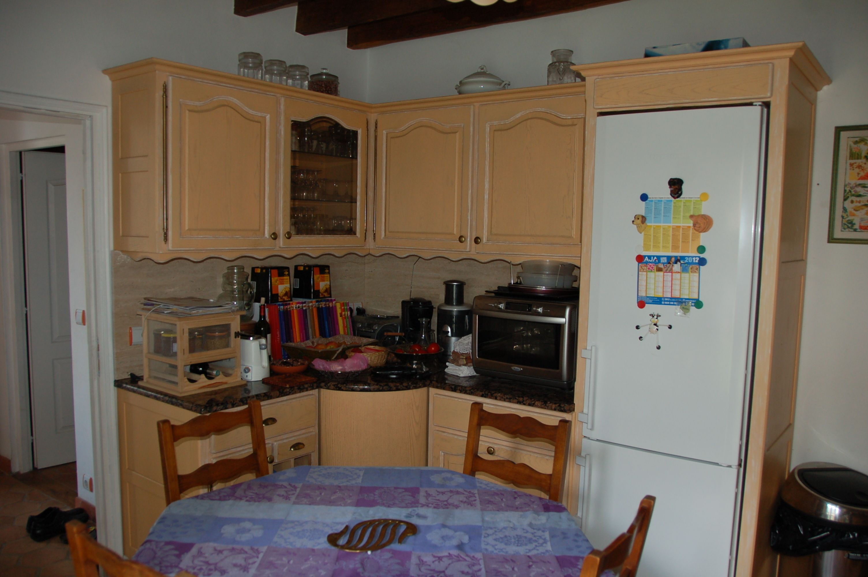 A kitchen with wooden cabinets, a refrigerator with magnets, a microwave, and a dining table with chairs.
