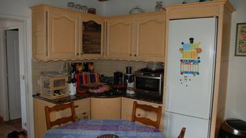A kitchen with wooden cabinets, a refrigerator with magnets, a microwave, and a dining table with chairs.