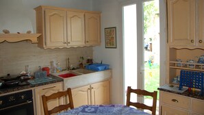 A kitchen with wooden cabinets, a sink, and a dining table with chairs. - Coffret d'Avenir (Saint-Denis-en-Val)