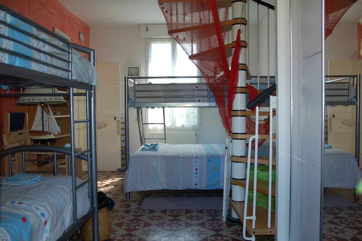 A dormitory room with bunk beds, a window with curtains, and a patterned floor.