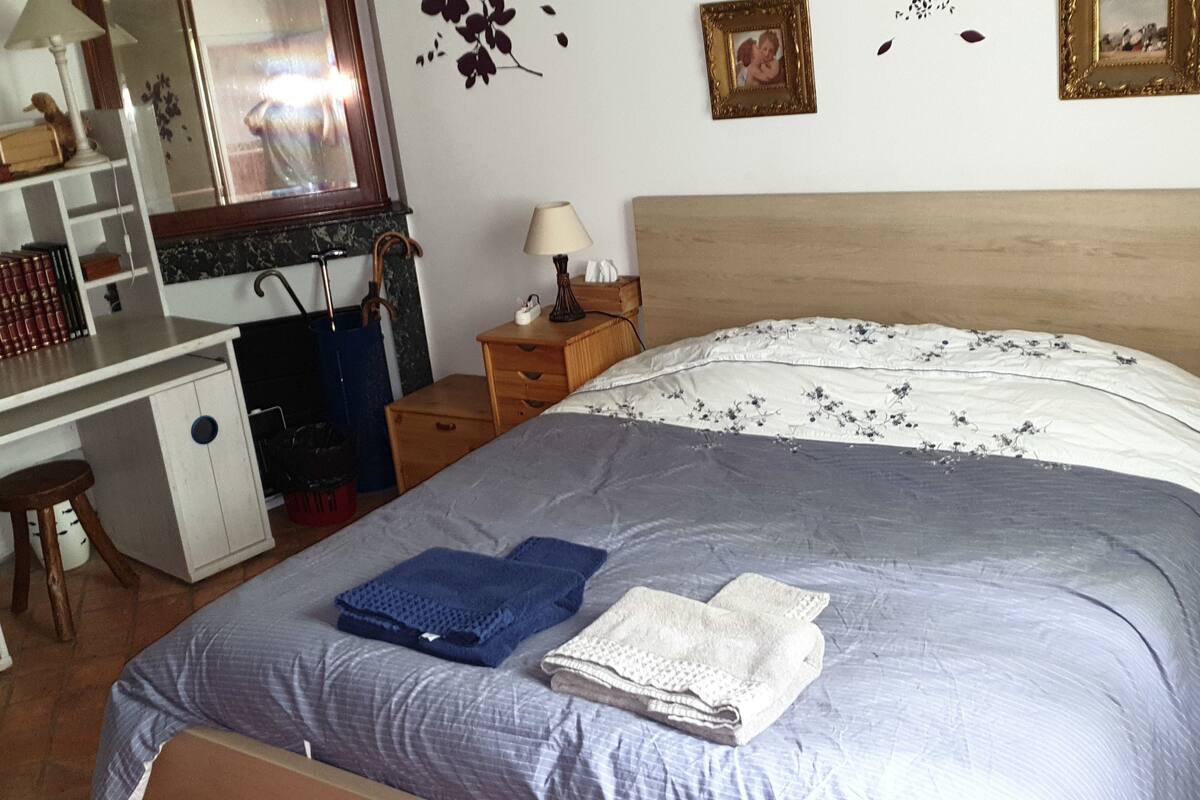 A bedroom with a bed, a desk, a chair, a dresser, and a small stool.