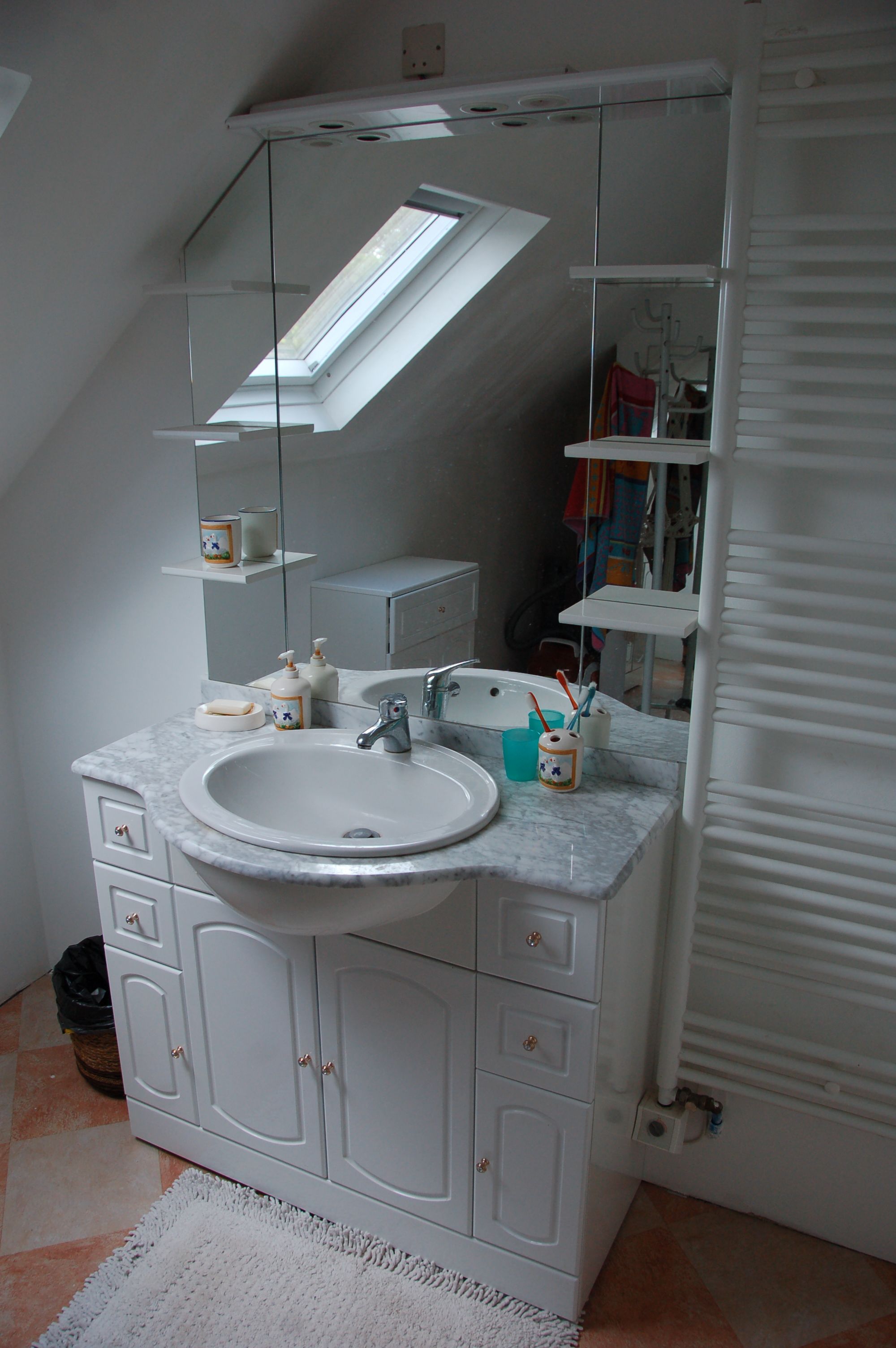 A bathroom with a white sink, mirror, and cabinets. There is a skylight above the sink, and a white radiator is visible to the right.