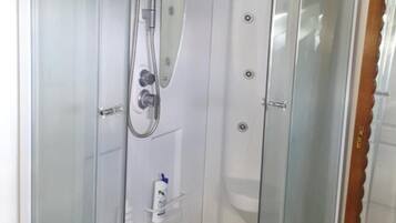 Douchecabine in hoekopstelling met een glazen deur, een handdouche en een inbouwkruk.