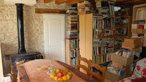 A cozy room with a wooden table set with fruit, a bookshelf filled with books, and a stone wall. - Coffret d'Avenir (Saint-Denis-en-Val)