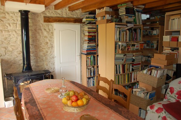 A cozy room with a wooden table set with fruit, a bookshelf filled with books, and a stone wall. - Coffret d'Avenir (Saint-Denis-en-Val)