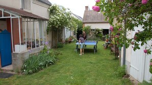 A backyard with a ping pong table, a glass-enclosed structure, and a garden with various plants and flowers. - Coffret d'Avenir (Saint-Denis-en-Val)
