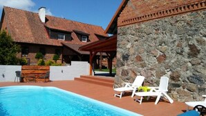 A swimming pool with lounge chairs, a stone wall, and a building with a tiled roof.