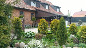 A two-story house with a brick facade, a wooden porch, and a garden with various plants and flowers.