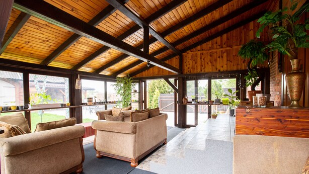 A spacious indoor area with wooden beams, a large sofa, and potted plants.