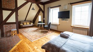 A bedroom with a bed, a TV, a window, a radiator, a brick wall, and a wooden ceiling.