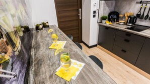 A modern kitchen with a wooden table set for a meal, featuring glasses of a yellow beverage, a coffee maker, and various kitchen utensils. - ApartMood (Katowice)