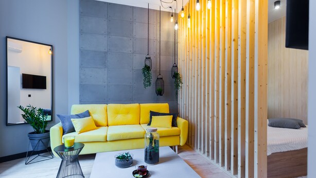 A modern living room with a yellow sofa, a white coffee table, and a bed with a wooden headboard. - ApartMood (Katowice)