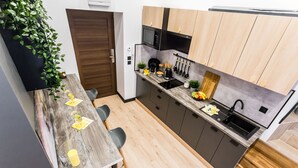 A modern kitchen with wooden cabinets, a black microwave, and a sink. - ApartMood (Katowice)