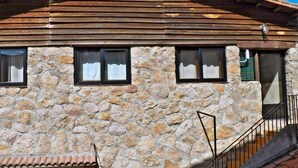 A stone building with wooden slats on the roof, three windows with curtains, and a metal railing. - Casa Rural Casona del Jerte (Jerte)