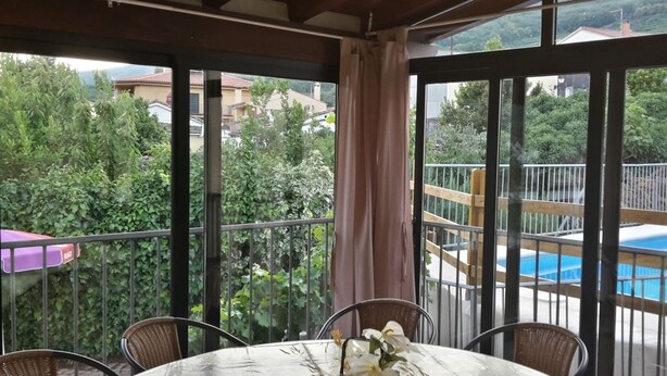 A balcony with a table and chairs, a view of a swimming pool, and surrounding greenery. - Casa Rural Casona del Jerte (Jerte)