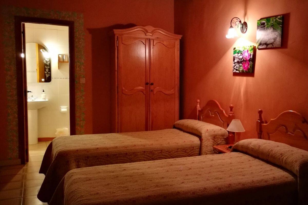 A room with two beds, a wardrobe, a wall-mounted light, and a framed picture.