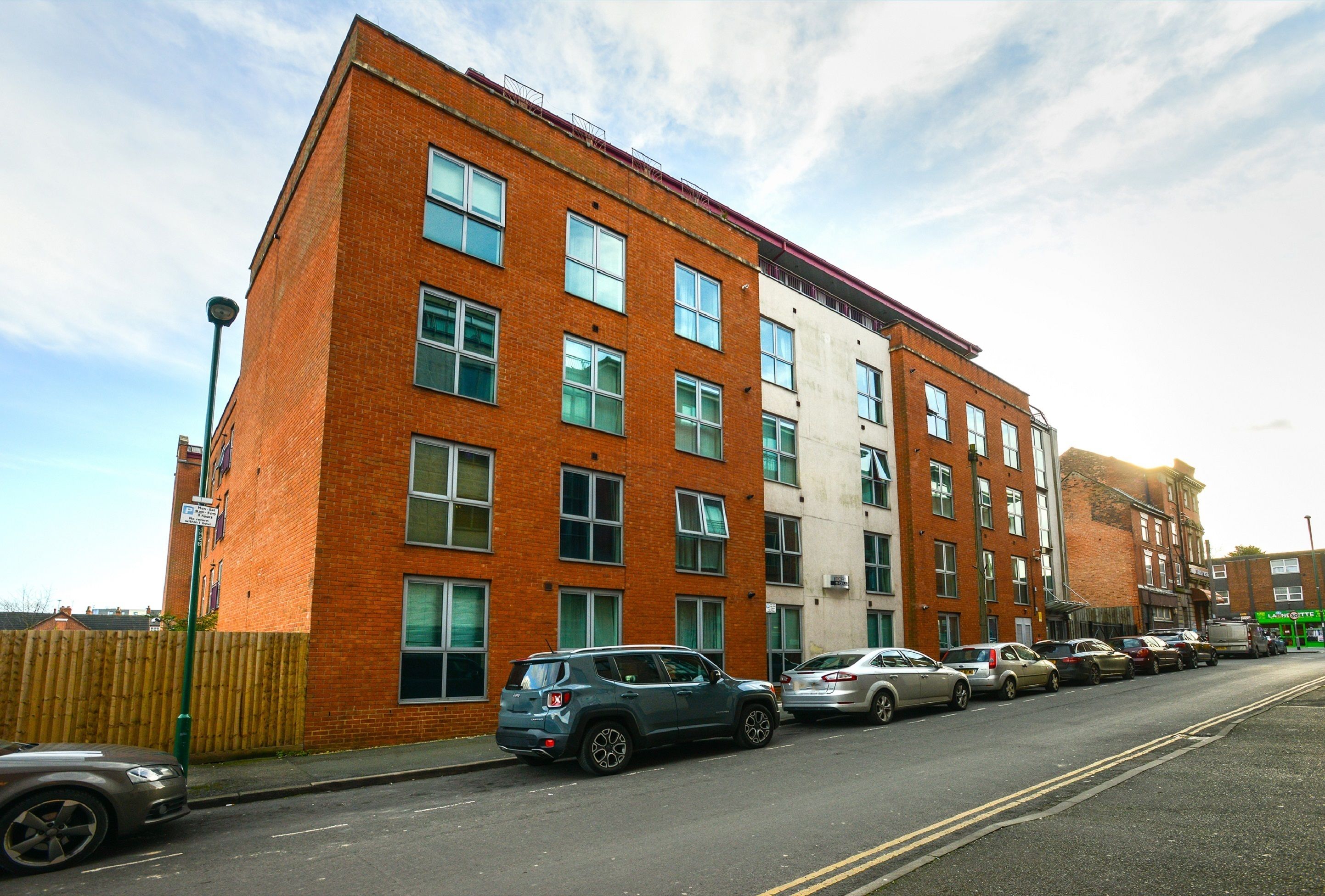 A multi-story brick building with several parked cars on the street in front.