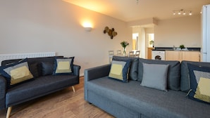 A modern living room with a grey sofa set, a dining area, and a kitchen in the background. - Portland Square (Nottingham)