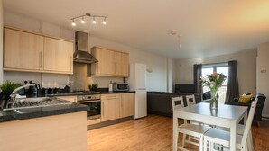 A modern kitchen with wooden cabinets, a stainless steel range hood, and a dining area with a white table and chairs. - Portland Square (Nottingham)