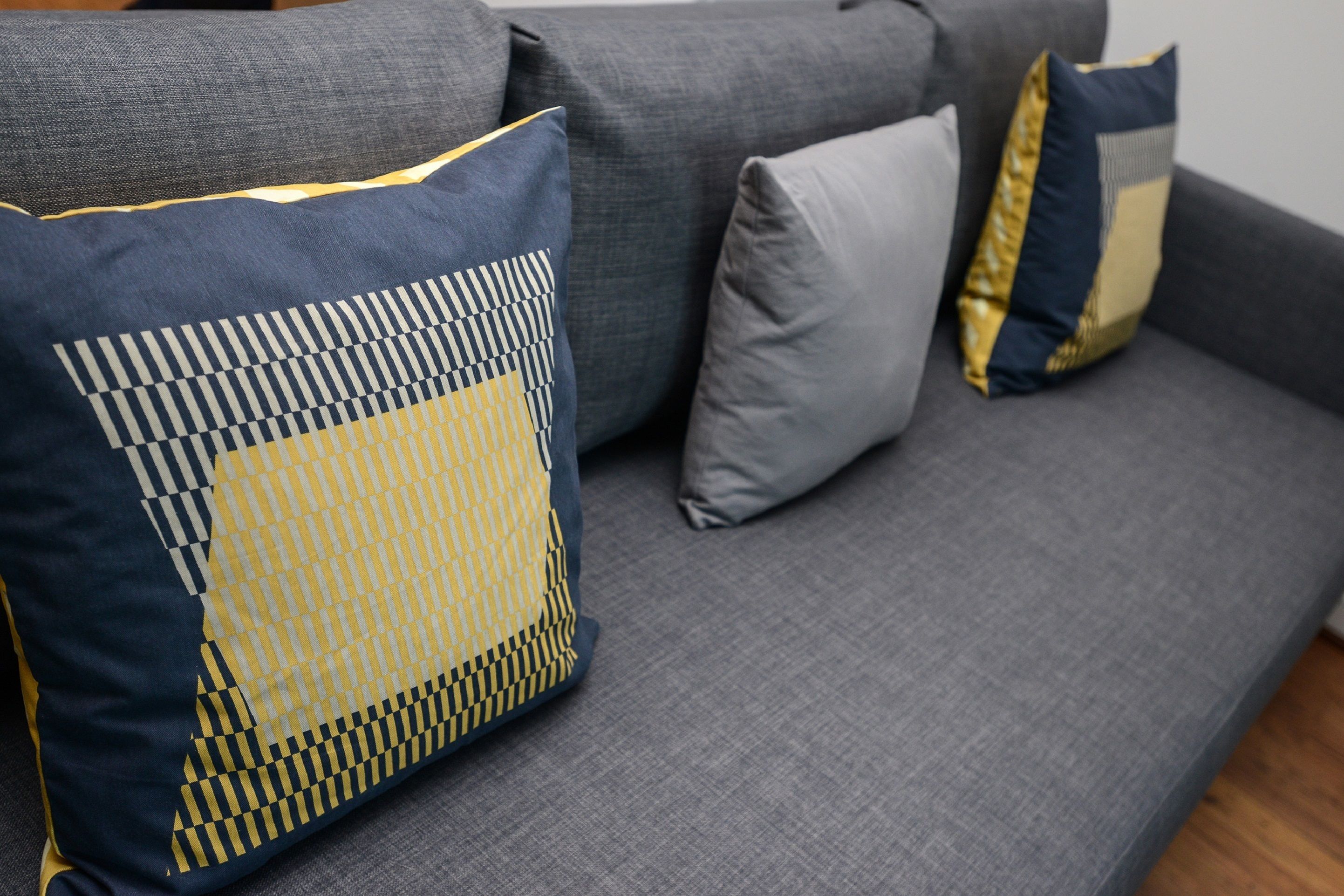A grey sofa with three cushions, one with a geometric pattern and two plain cushions.