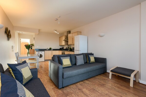 A compact living space with a sofa, a bench, a dining table, and a kitchenette.
