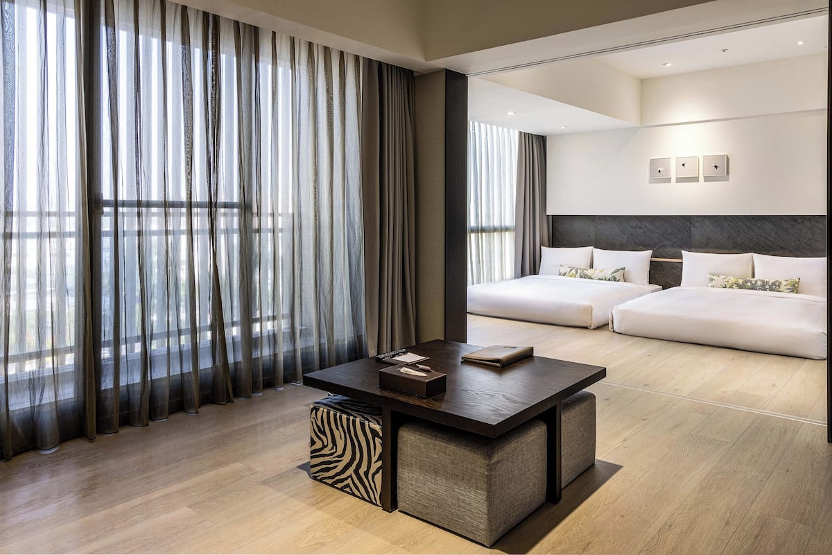 A modern hotel room with a large bed, a desk with a chair, and sheer curtains.