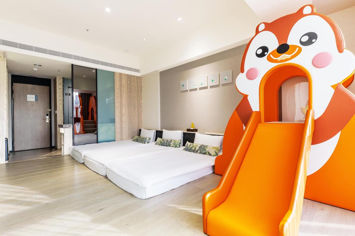 A modern hotel room with a large bed, a sofa, a small table, and a playful orange slide.