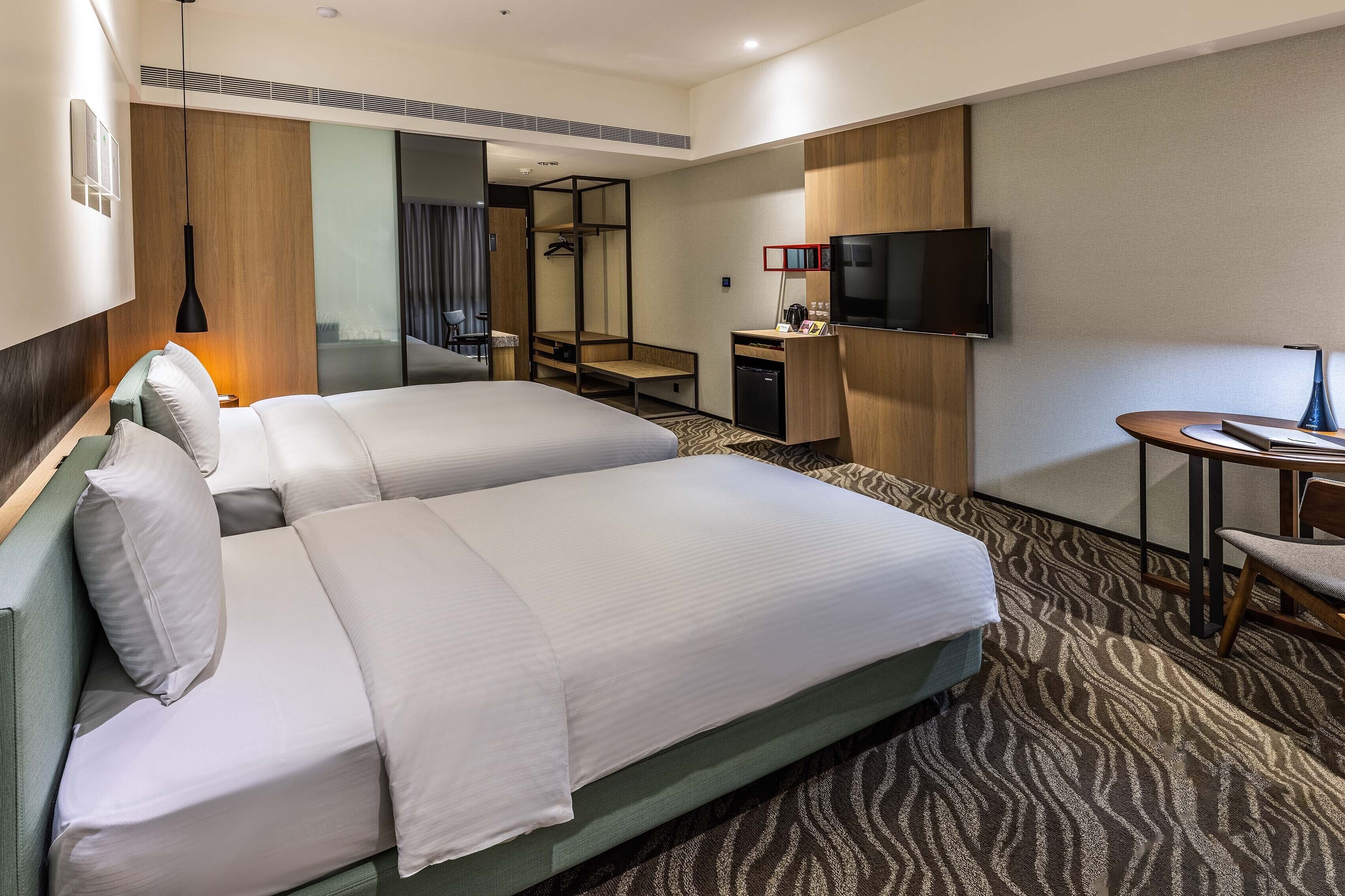 Una habitación de hotel con dos camas, un escritorio, un televisor y una mesita.
