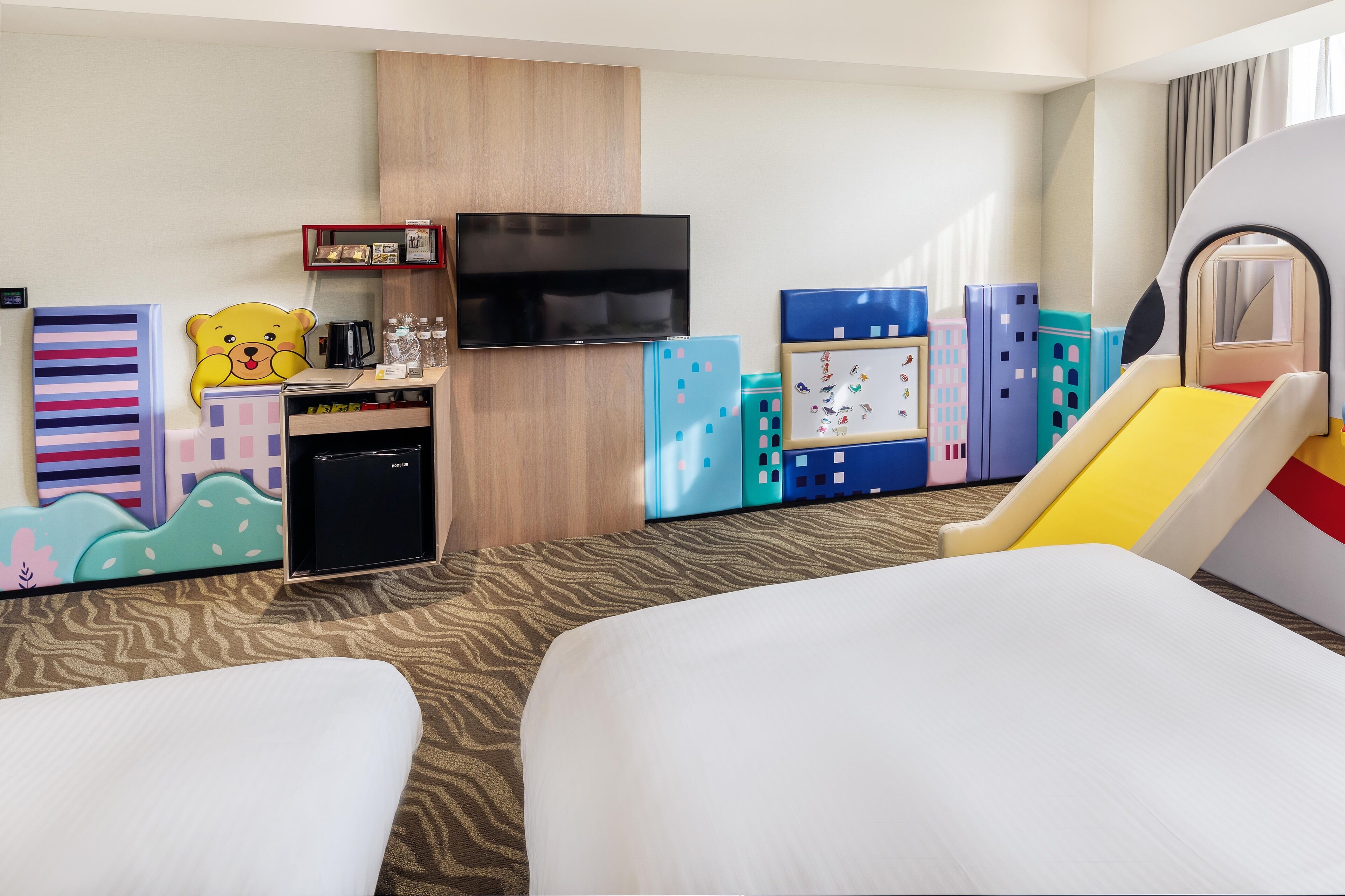 Une chambre d’hôtel équipée d’un lit, d’une télévision, d’une petite kitchenette et d’un espace de jeux pour enfants.
