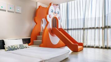 A modern hotel room with a large bed, a playful orange slide, and a view of the city through sheer curtains.